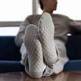A person reclining on a blue couch with their legs raised, wearing light gray textured knit socks and matching lounge pants in a bright indoor setting. thumbnail