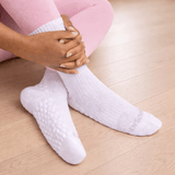 White ribbed ankle socks with textured grip dots on the sole, worn by a person sitting on a light wood floor.
