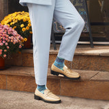 A person wearing light blue trousers, beige loafers with gold chain detailing, and blue patterned socks, standing on stone steps outdoors next to potted flowers. thumbnail