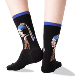 A pair of black crew socks with blue ribbed cuffs, featuring a printed portrait of Vermeer's Girl with a Pearl Necklace on the sides, shown on a person's feet against a white background.
