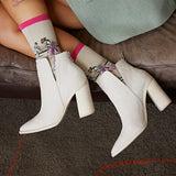 A person seated on a brown leather bench wearing off-white ankle boots with block heels and patterned socks featuring a pink cuff. thumbnail