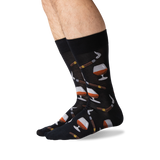 A pair of black crew socks with a pattern of whiskey glasses, cigars, and cigars being lit by matches, shown on a person's legs against a white background. thumbnail