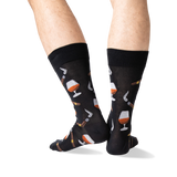 A pair of black crew socks with a pattern of whiskey glasses, cigars, and cigars being lit, shown on a person's legs against a white background.