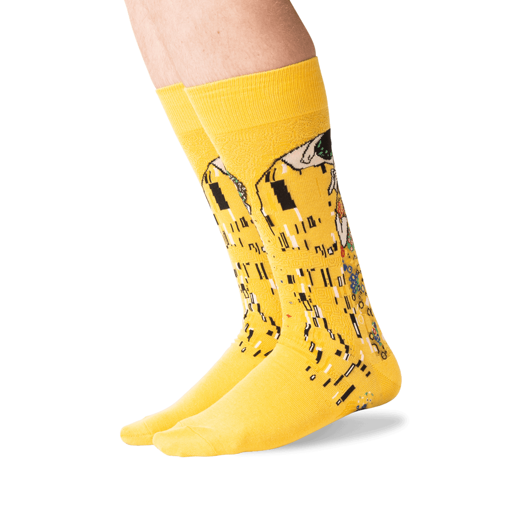 A pair of bright yellow crew socks with a stylized piano-key and figure graphic in black, white, and gray, worn on a person's feet against a clean white background.
