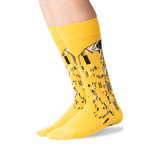 A pair of bright yellow crew socks with a stylized piano-key and figure graphic in black, white, and gray, worn on a person's feet against a clean white background.