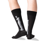 A pair of black crew socks worn on a person's legs, featuring a large white sculpture design on the side of each sock, photographed against a clean white background.