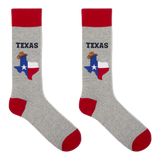 A pair of crew socks in heather gray with red cuffs, heels, and toes. Each sock features a graphic of the state of Texas filled with the Texas flag and a small cowboy hat, with the word 'TEXAS' printed above in dark blue.