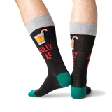 A pair of novelty crew socks worn on a person's legs, featuring a dark charcoal body with a gray cuff, green heels and toes, red text reading 'JOLLY AF', and a small cocktail graphic on the upper calf. thumbnail