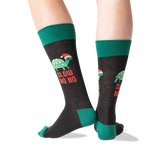 A pair of crew socks worn on a person's legs, featuring a dark charcoal gray body with green cuffs, heels, and toes, and a graphic of a green turtle wearing a red Santa hat with the text 'SLOW HO HO' in red. thumbnail