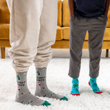 Two people wearing festive socks with holiday-themed designs on a carpeted floor. thumbnail