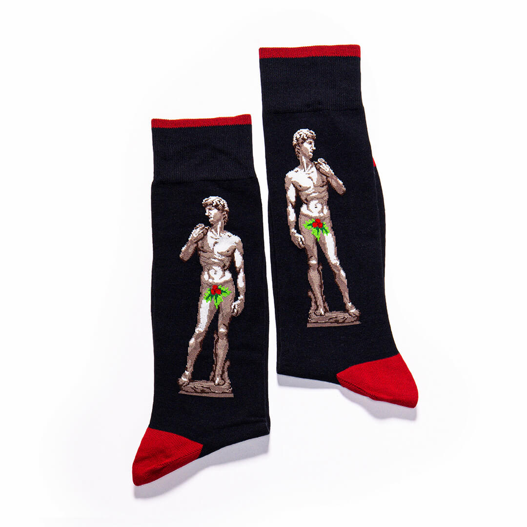 A pair of black crew socks with red cuffs, heels, and toes, featuring a graphic print of Michelangelo's David statue with a green bow-tie overlay.