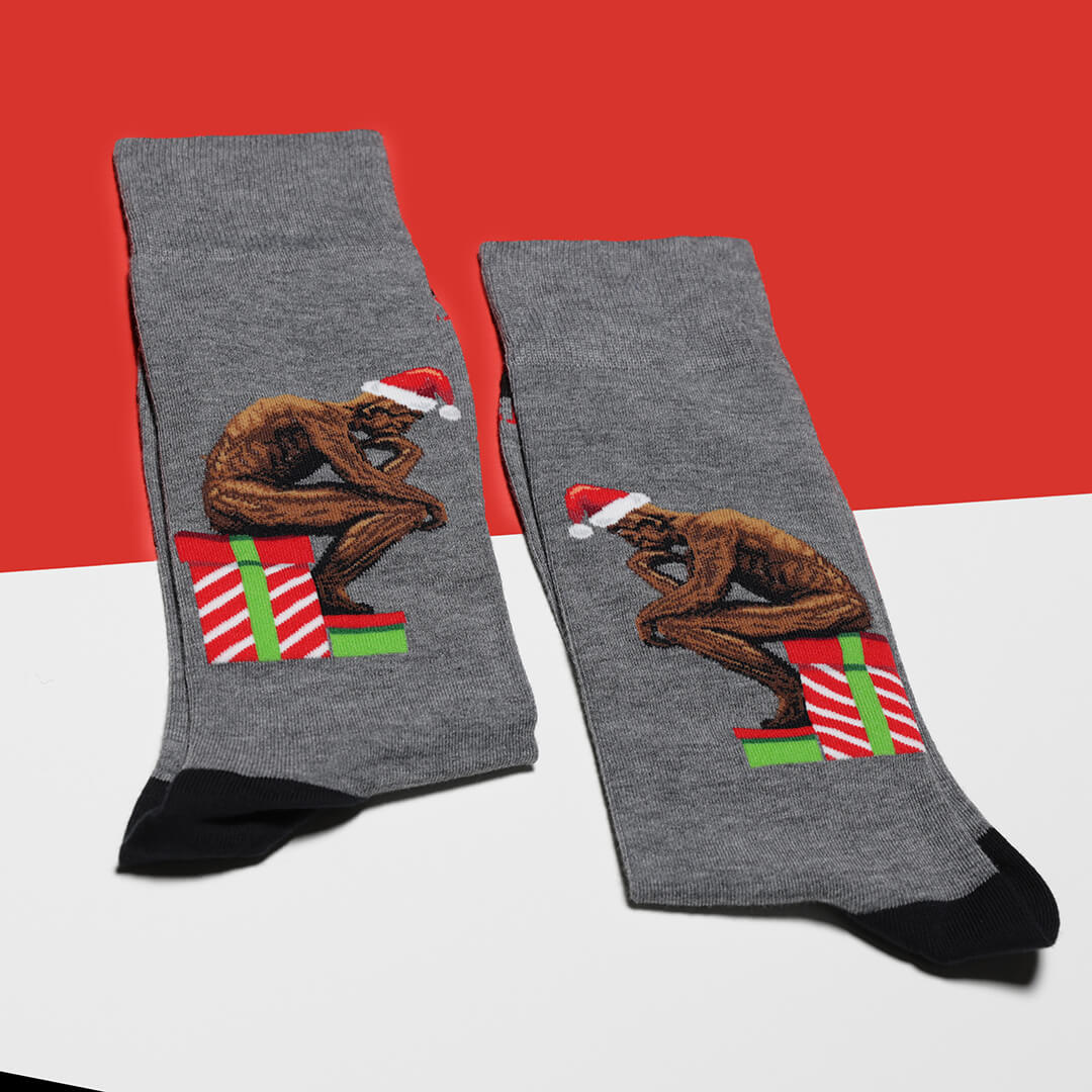 Gray socks with a Christmas-themed design of The Thinker on a red and white background