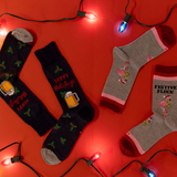 Two pairs of socks with festive designs on a red surface with Christmas lights.