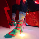 Person wearing festive socks with Christmas lights on a red couch.