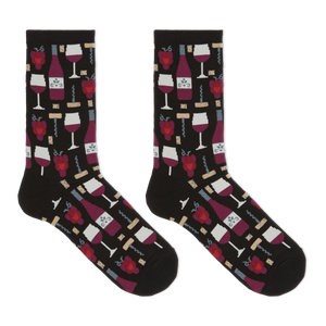 A pair of crew socks on a plain white background, featuring a black base with a repeating pattern of red wine bottles, wine glasses, corkscrews, and red raspberries.