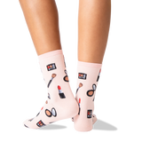 A pair of light pink crew socks with a makeup-themed print, worn on a person's feet against a clean white background.
