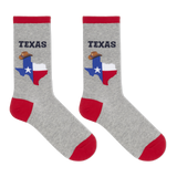A pair of heather gray crew socks with red cuffs, heels, and toes. Each sock features a graphic of the state of Texas filled with the Texas flag and a cowboy hat, with the word 'TEXAS' printed above in dark navy. thumbnail