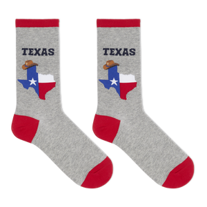 A pair of heather gray crew socks with red cuffs, heels, and toes. Each sock features a graphic of the state of Texas filled with the Texas flag and a cowboy hat, with the word 'TEXAS' printed above in dark navy.