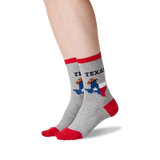 A pair of crew socks worn on a person's feet, shown against a plain white background. The socks are heather gray with red toes, heels, and cuffs, featuring a graphic of the state of Texas with a football player and the text 'TEXAS'. thumbnail