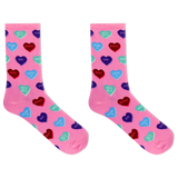 A pair of pink crew socks with an all-over pattern of colorful heart candies in red, blue, purple, and green, each printed with Valentine's themed phrases like 'Kiss Kiss', 'Love You', and 'HUGS'.