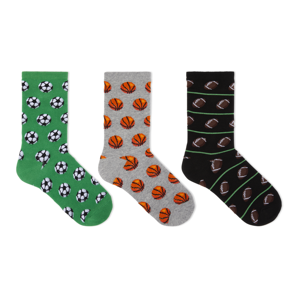 Three pairs of crew socks displayed side by side on a plain white background. The left pair is green with black and white soccer ball patterns, the middle pair is gray with orange basketball patterns, and the right pair is black with brown football patterns and thin green stripes.