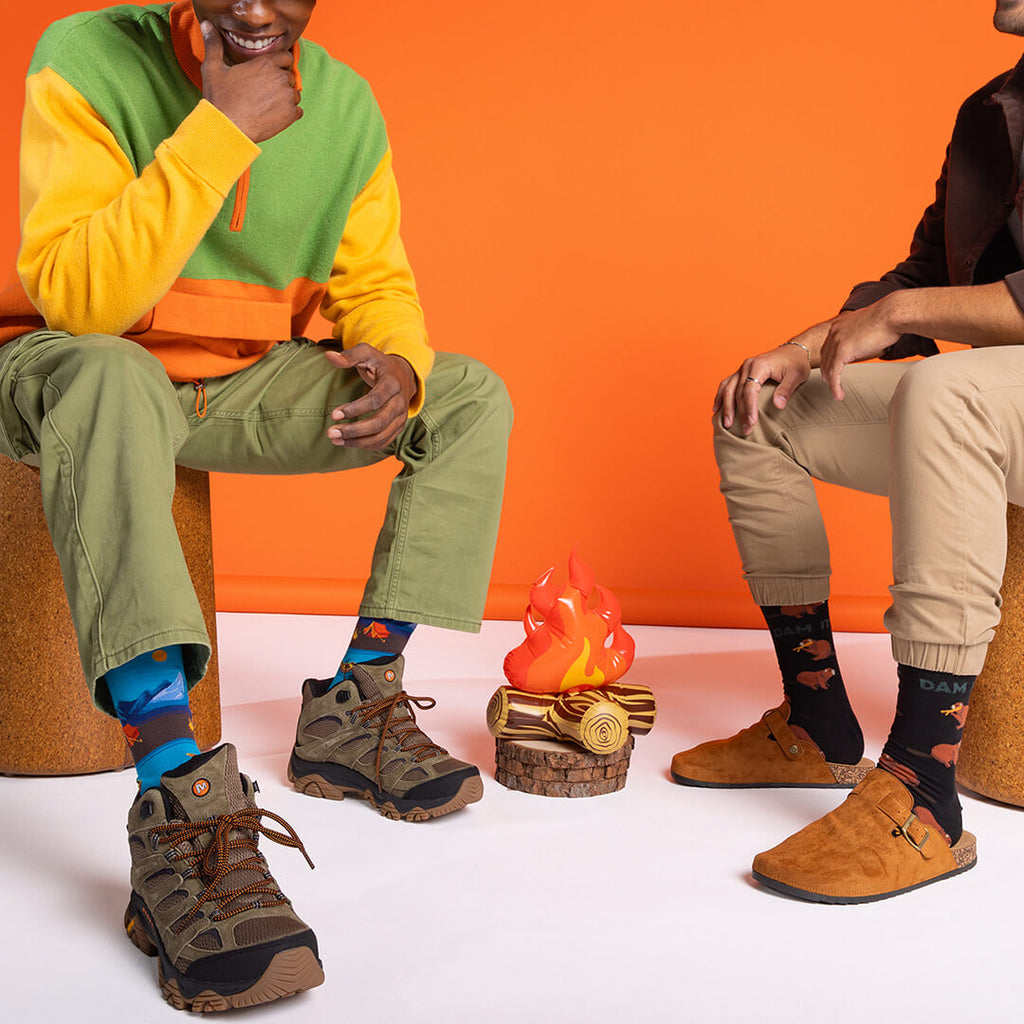 Two people sitting on stools with colorful socks and shoes, wearing patterned socks.