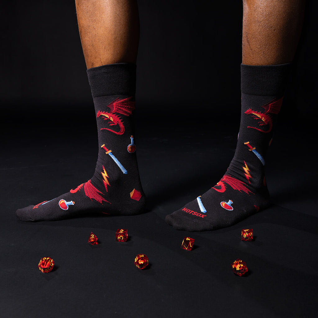 Black socks with red dragons, potions, and sword designs worn by a person on a black background