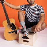 Person sitting with a guitar, wearing striped shirt and colorful socks against an orange background thumbnail