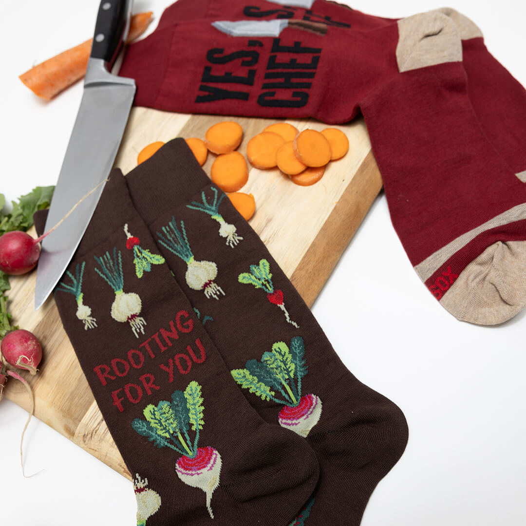 Brown socks with vegetable designs and text on a cutting board with carrots and a knife.