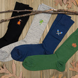 Four pairs of socks in black, gray, blue, and green with embroidered designs on a wooden surface. thumbnail