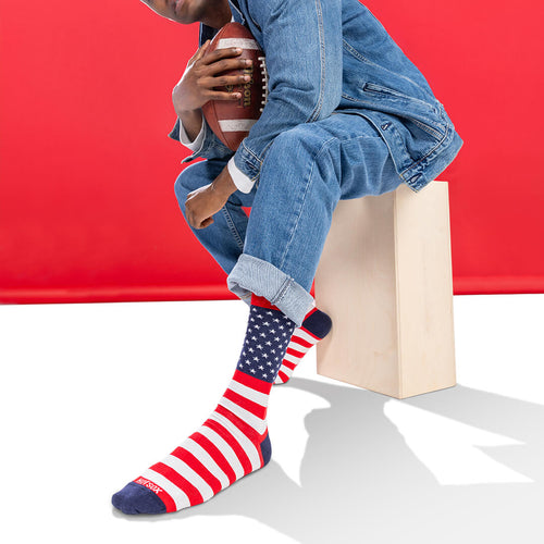 Person wearing American flag socks sitting on a box against a red background
