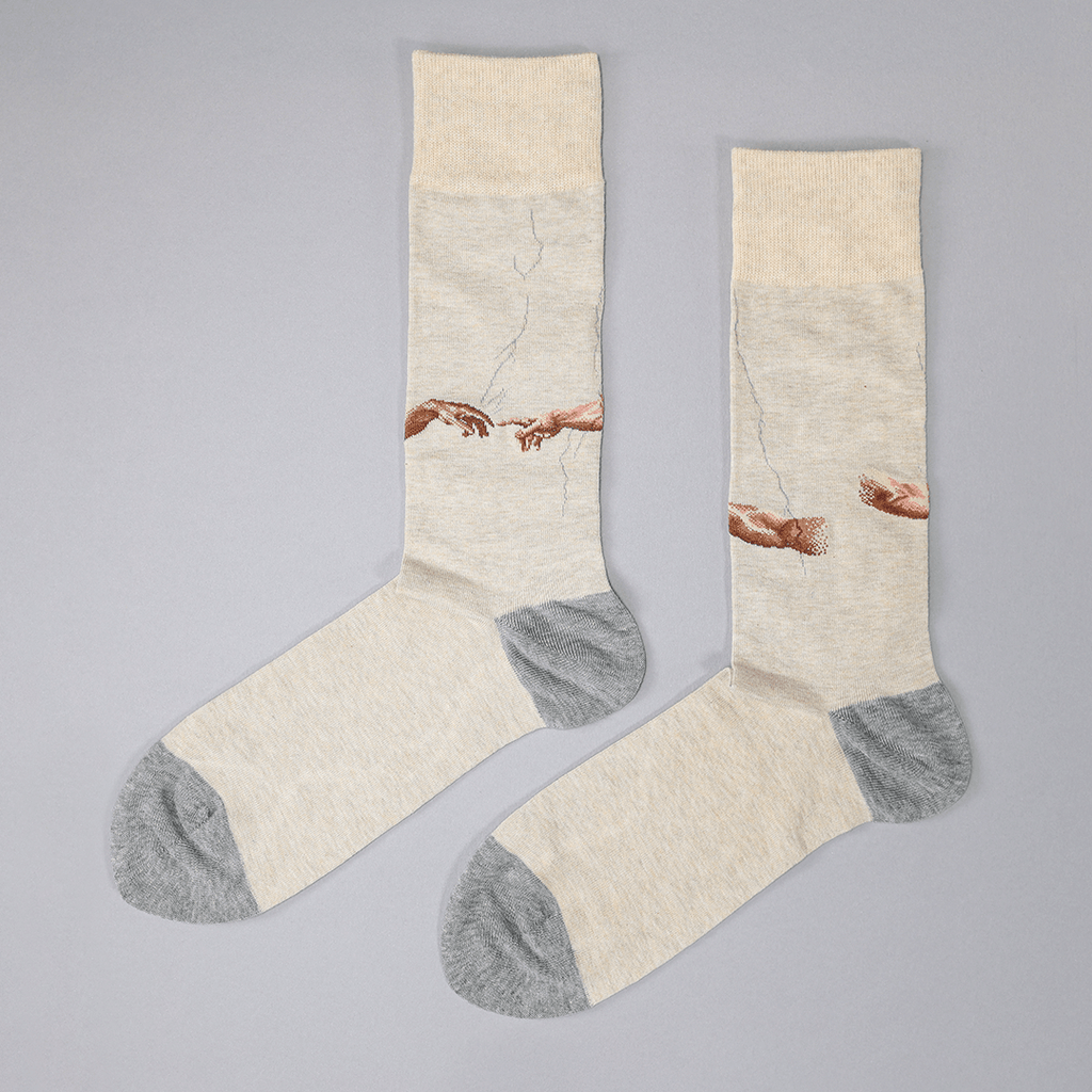 A pair of crew socks with a beige and gray color-blocked design, featuring a printed graphic of two hands reaching toward a crack in the wall, styled on a neutral gray background.