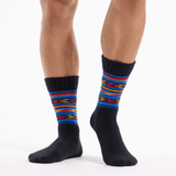 A pair of crew socks worn on a person's feet, featuring a black base with a vibrant multicolor striped pattern in red, blue, yellow, and orange around the calf. thumbnail