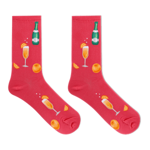 A pair of bright pink crew socks featuring a festive champagne-themed print with orange slices, champagne glasses, and a green champagne bottle, displayed against a solid white background.