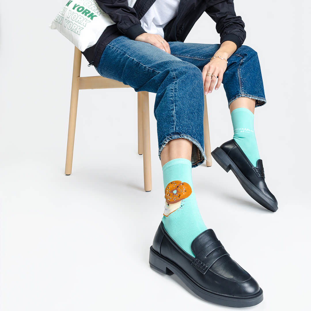 Person wearing light blue socks with a donut design, sitting on a chair.
