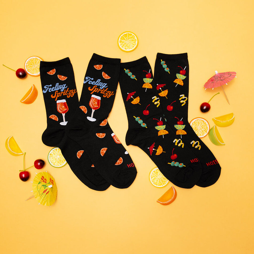 Two pairs of black socks with colorful designs on a yellow background with lemon slices and cocktail umbrellas.