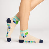 A pair of ankle socks worn on a model's feet, shown against a clean light gray studio background. The socks are heather beige with a colorful geometric heart design in blue, green, and navy on the ankle, striped bands in blue, green, and white on the sides, and solid navy heels, toes, and cuffs. thumbnail