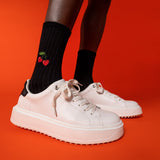 White sneakers worn with black socks featuring red cherries on a red background