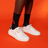 White sneakers worn with black socks featuring a cherry design on an orange background thumbnail