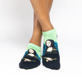 A person's feet wearing low-cut socks featuring a split design: light green on the upper half and black on the lower half, with a printed portrait of the Mona Lisa on the front.