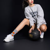 Person wearing a gray sweatshirt and white sneakers with a basketball on a black background