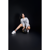 Woman in gray sweatshirt, white sneakers  and basketball socks holding a black basketball on a black background