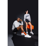 Two people sitting on a black background wearing matching outfits with orange basketball socks.
