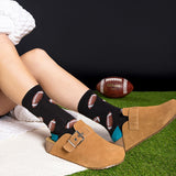 Person wearing black socks with football patterns, sitting on grass with a Wilson football in the background. thumbnail