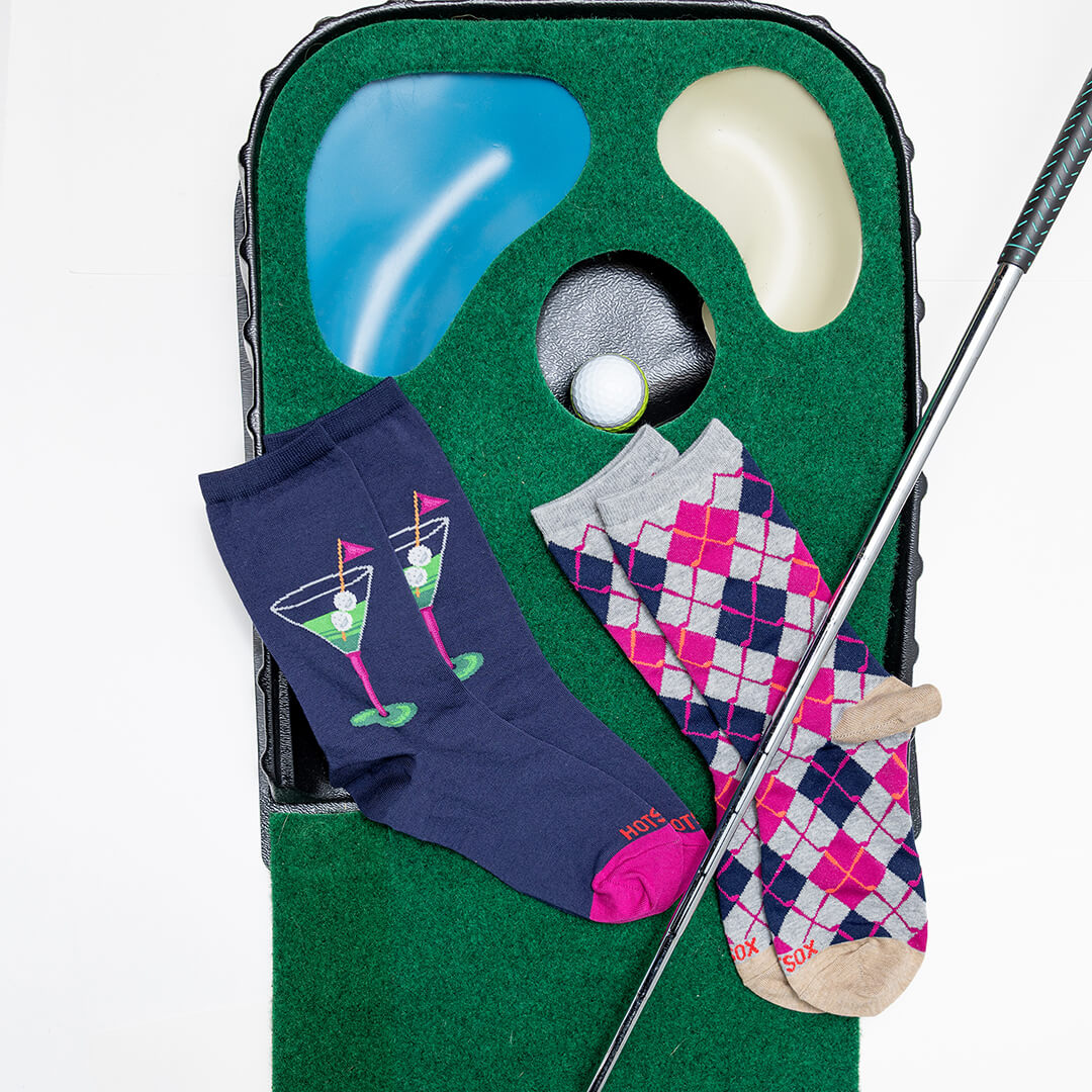 Two pairs of socks with golf-themed designs on a green golf simulator mat.