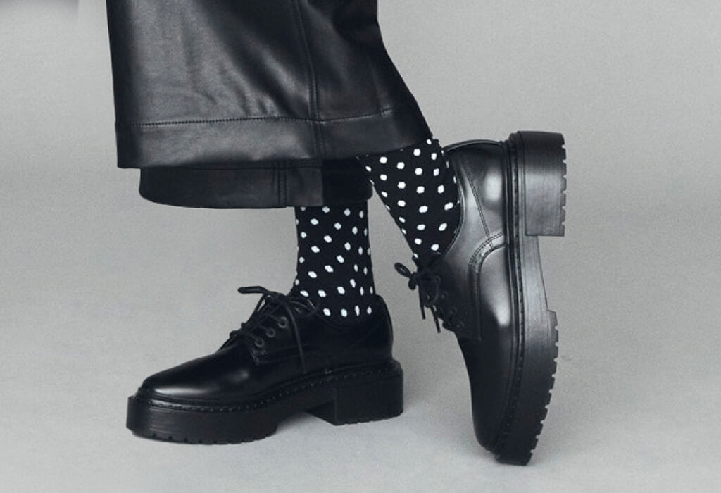 Black leather boots and polka dot socks on a neutral background