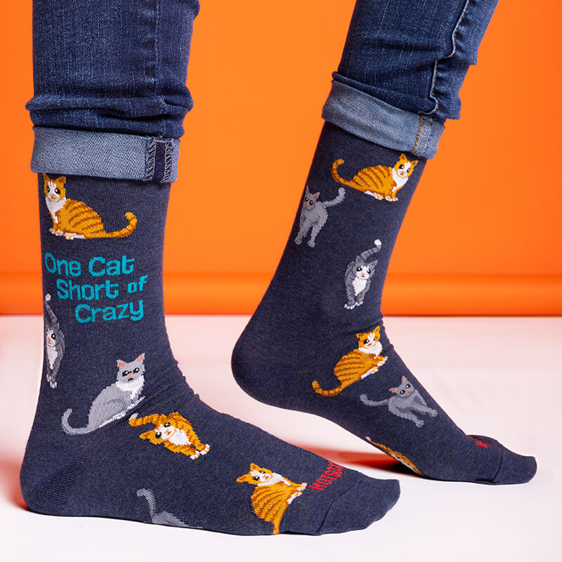 Navy socks with cat illustrations and text worn by a person on an orange background