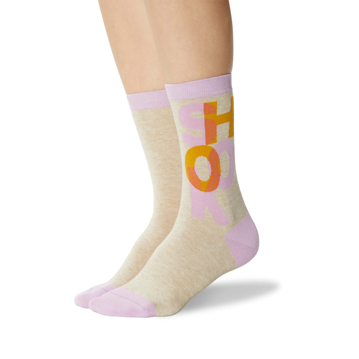 A pair of crew socks worn on a model's feet, featuring a heather beige body with a lavender ribbed cuff and toe, and a graphic design of the word 'SHOOK' in orange and pink.