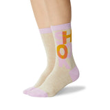 A pair of crew socks worn on a model's feet, featuring a heather beige body with a lavender ribbed cuff and toe, and a graphic design of the word 'SHOOK' in orange and pink.