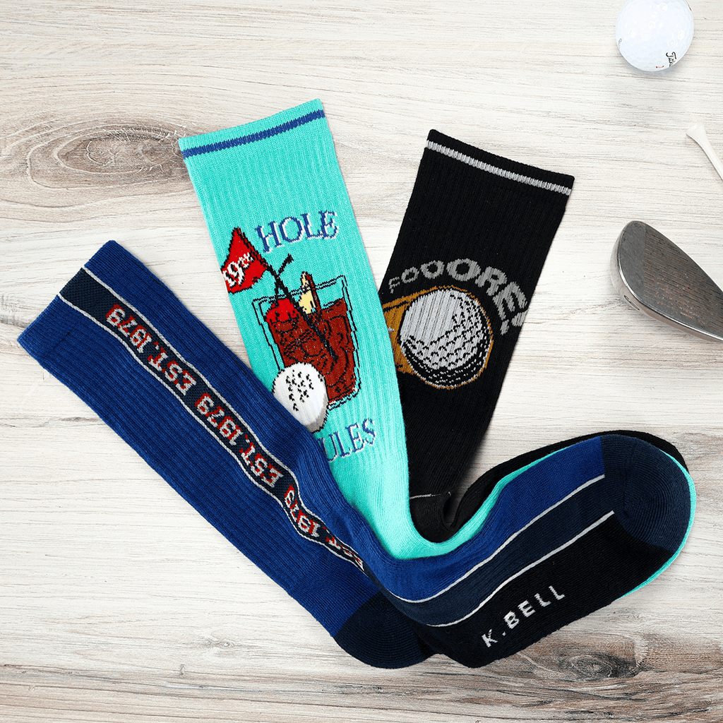 Three pairs of golf-themed socks on a wooden surface with a golf club in the background.
